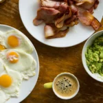 cholesterol on carnivore diet. Close-up of bacon, sunny side eggs, and guacamole on a wooden surface — foods commonly associated with cholesterol in a carnivore diet.